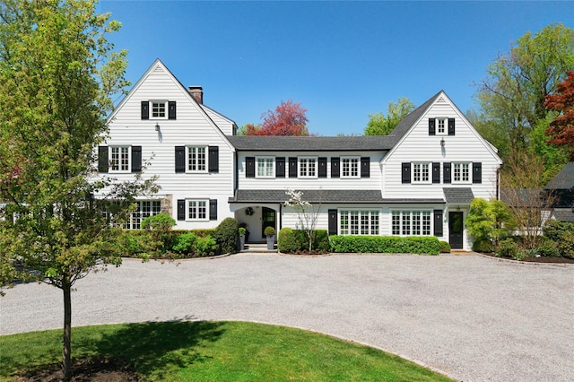 view of front of home with a chimney, gravel driveway, and a shingled roof