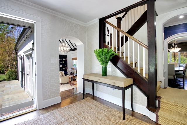 foyer entrance with a chandelier, arched walkways, ornamental molding, wood finished floors, and baseboards