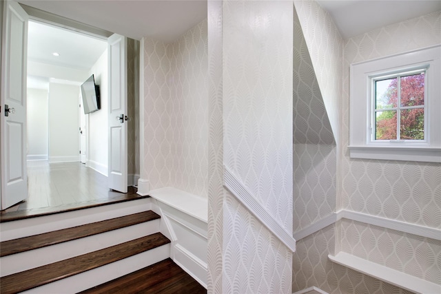 stairway with wallpapered walls, wood finished floors, and baseboards