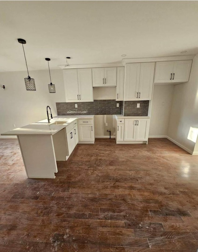 kitchen with dark wood-style flooring, a sink, a peninsula, white cabinetry, and tasteful backsplash