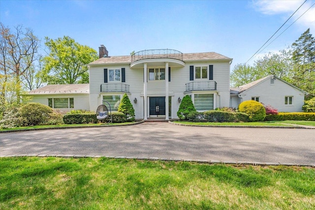 neoclassical home featuring driveway, a chimney, and a balcony