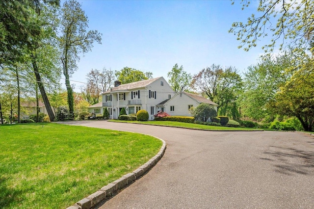 colonial-style house featuring a chimney, curved driveway, and a front lawn