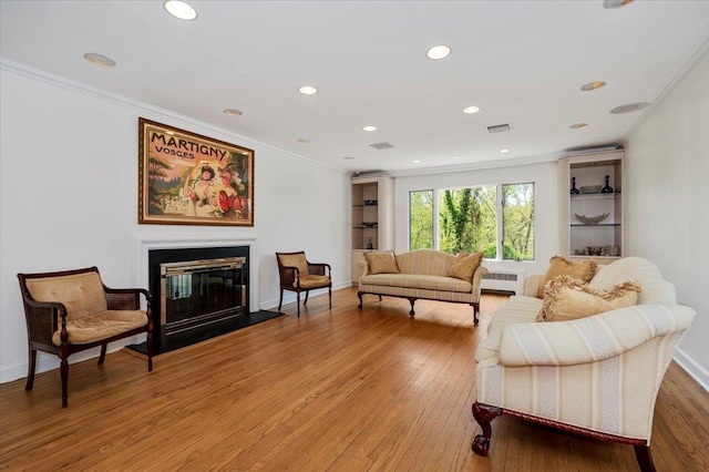 living area with ornamental molding, a glass covered fireplace, light wood-style flooring, and visible vents