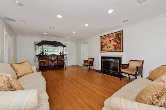 living room with recessed lighting, light wood-style floors, ornamental molding, and a glass covered fireplace