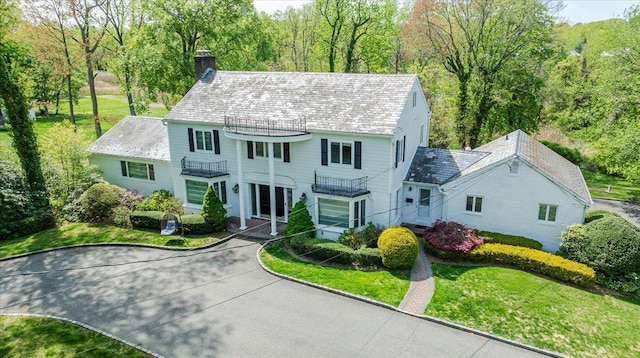 colonial house with a chimney, a balcony, a high end roof, and a front yard