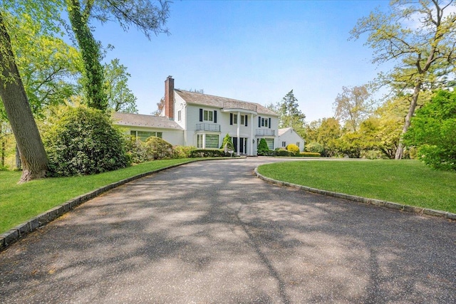 colonial inspired home featuring a chimney, a front yard, and curved driveway