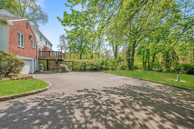 view of community featuring an attached garage, a yard, a deck, and aphalt driveway