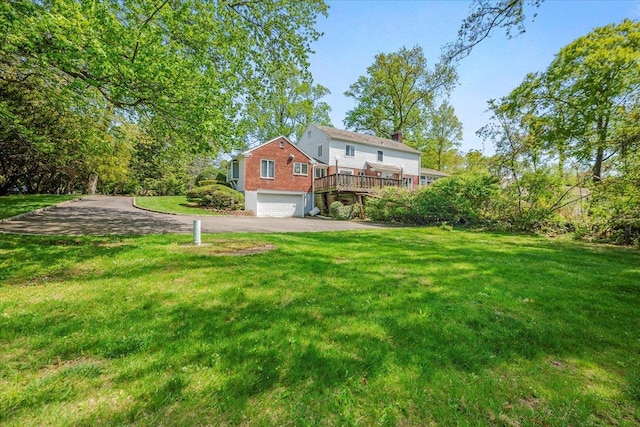 view of yard with a deck, a garage, and driveway