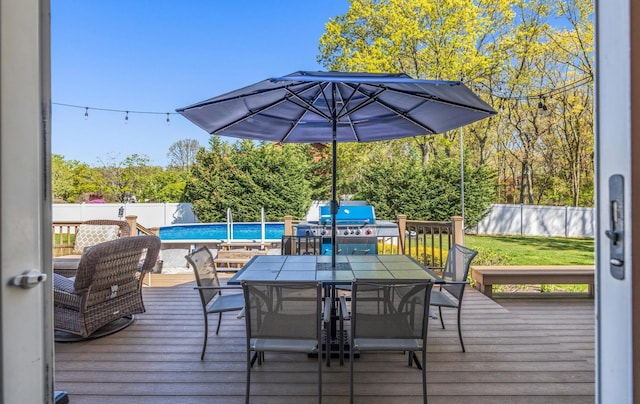 deck featuring a fenced backyard, a fenced in pool, outdoor dining space, and a grill