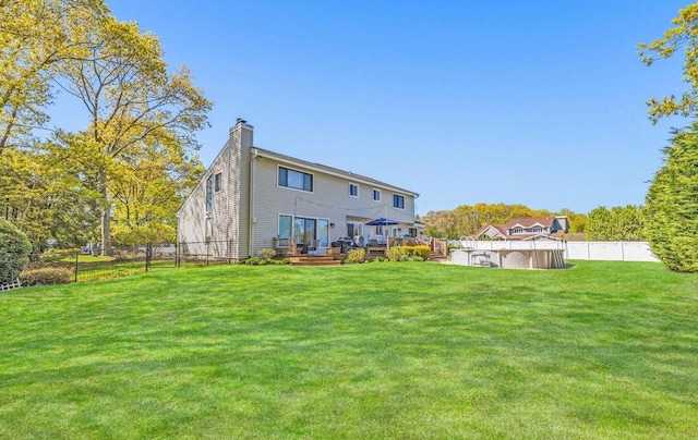 back of property featuring a chimney, fence, a wooden deck, a yard, and a fenced in pool