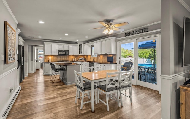 dining area featuring ornamental molding, a wealth of natural light, a baseboard radiator, and light wood-style floors