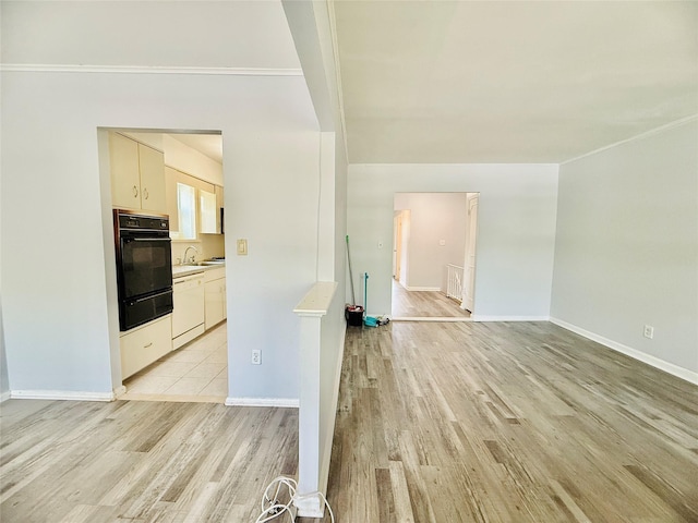 interior space with baseboards, a sink, light wood-style flooring, and crown molding