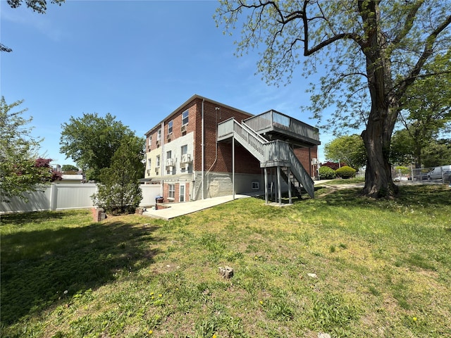 back of house with fence, brick siding, a wooden deck, stairway, and a lawn