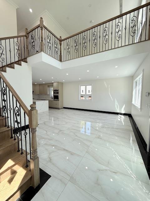 interior space with crown molding, a towering ceiling, baseboards, and marble finish floor