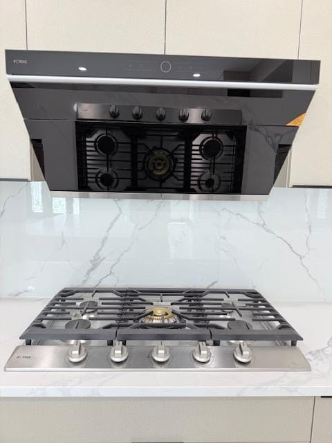 room details with stainless steel gas stovetop, light stone counters, and decorative backsplash