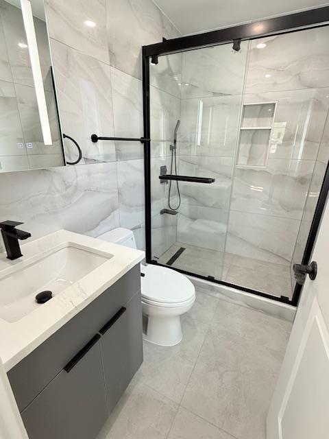 full bath with vanity, toilet, marble finish floor, tile walls, and a shower stall