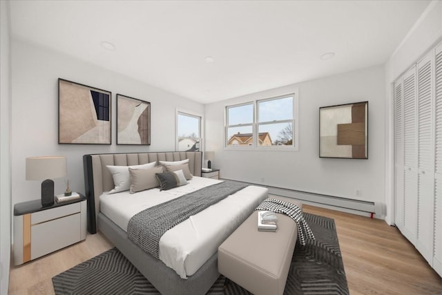 bedroom with a closet, light wood-style floors, baseboard heating, and recessed lighting