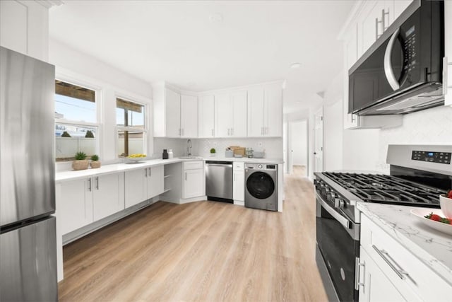 kitchen featuring stainless steel appliances, washer / dryer, backsplash, light wood-style flooring, and a sink