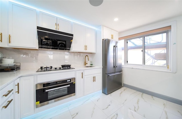 kitchen with a sink, appliances with stainless steel finishes, white cabinetry, and marble finish floor
