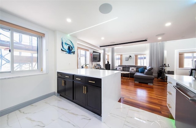 kitchen with dark cabinetry, light countertops, marble finish floor, a healthy amount of sunlight, and stainless steel dishwasher