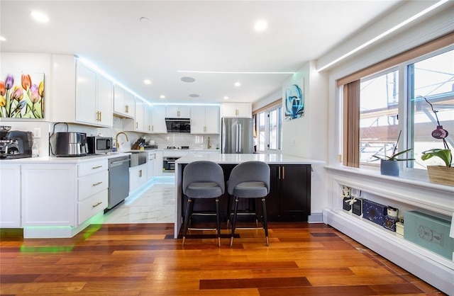 kitchen with a kitchen bar, light countertops, white cabinetry, a sink, and stainless steel appliances