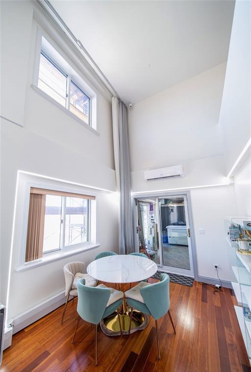 dining space with a high ceiling, a wall unit AC, wood finished floors, and a wealth of natural light