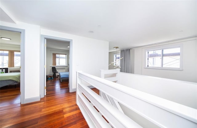 corridor featuring baseboards, an upstairs landing, and wood finished floors