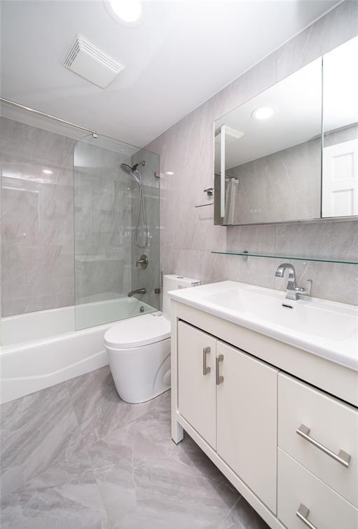 bathroom featuring visible vents, vanity, toilet, bathing tub / shower combination, and tile walls