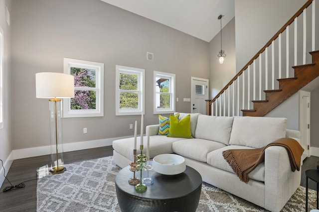 living area featuring baseboards, high vaulted ceiling, wood finished floors, and stairway