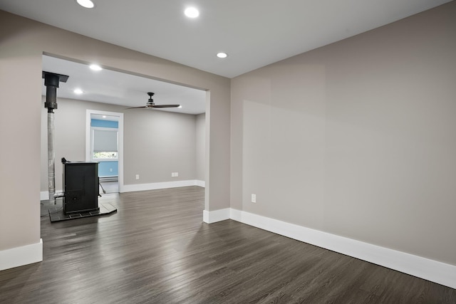 unfurnished living room with baseboards, ceiling fan, a wood stove, and dark wood-style floors