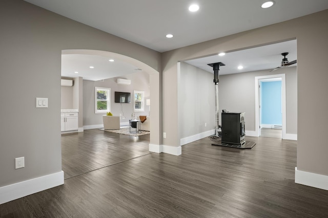 unfurnished living room with arched walkways, a wall unit AC, a wood stove, and dark wood-type flooring