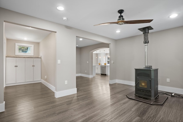 unfurnished living room featuring baseboards, a wood stove, ceiling fan, and wood finished floors