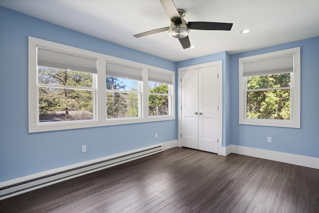 unfurnished bedroom featuring a closet, a baseboard radiator, multiple windows, and dark wood-style floors
