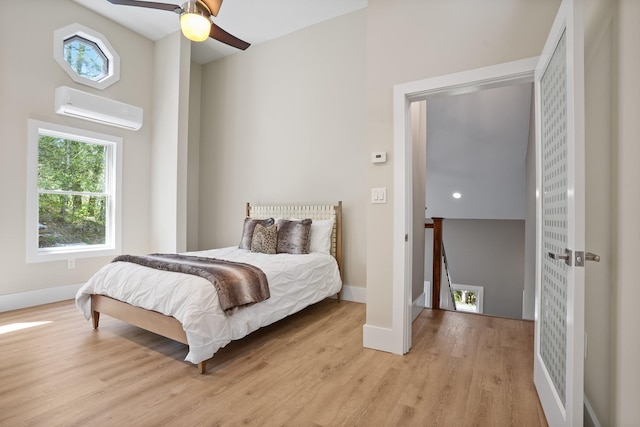bedroom with baseboards, a wall unit AC, multiple windows, and light wood-type flooring