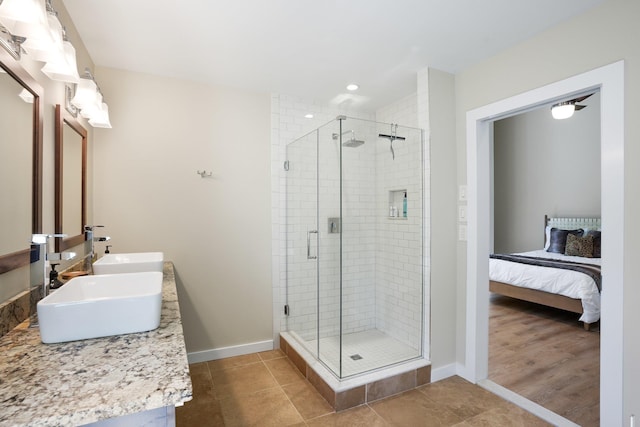 bathroom featuring a sink, double vanity, baseboards, a shower stall, and ensuite bathroom