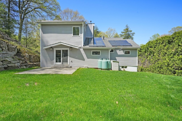 rear view of property featuring a lawn, solar panels, a chimney, and a patio area