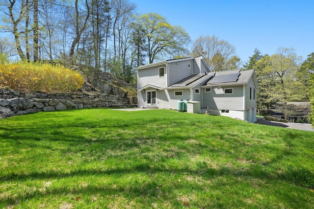 rear view of house with a lawn, a garage, roof mounted solar panels, and entry steps