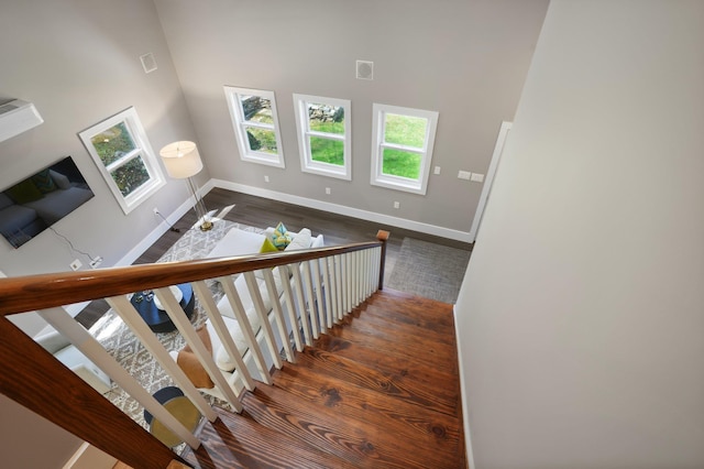 stairway featuring wood finished floors, baseboards, a high ceiling, and visible vents