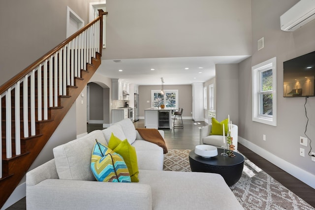 living room with an AC wall unit, plenty of natural light, wood finished floors, and a towering ceiling