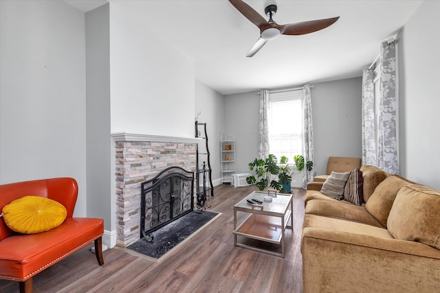 living area with baseboards, a stone fireplace, a ceiling fan, and wood finished floors