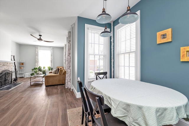 dining area featuring a brick fireplace, baseboards, ceiling fan, and wood finished floors
