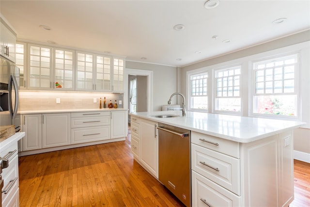 kitchen featuring light wood-type flooring, white cabinetry, tasteful backsplash, a sink, and appliances with stainless steel finishes