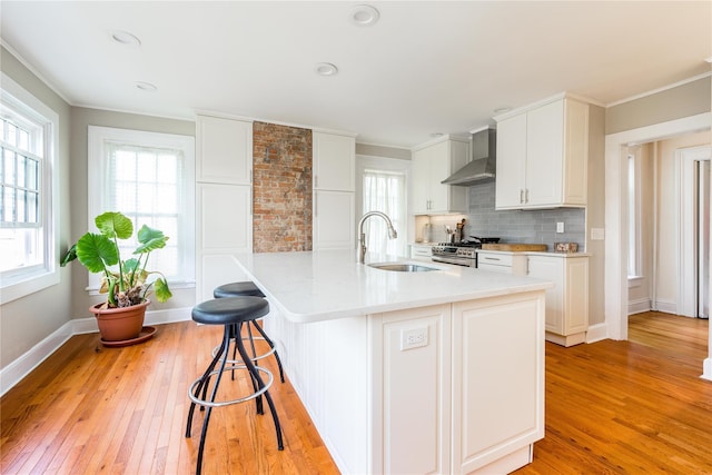 kitchen with crown molding, a kitchen breakfast bar, wall chimney exhaust hood, a sink, and light wood-style flooring