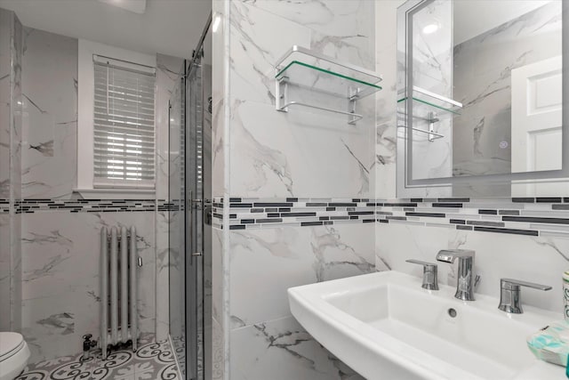 full bath featuring a sink, toilet, a marble finish shower, radiator heating unit, and tile walls
