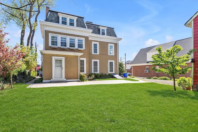 view of front of house featuring stucco siding, mansard roof, a high end roof, and a front lawn