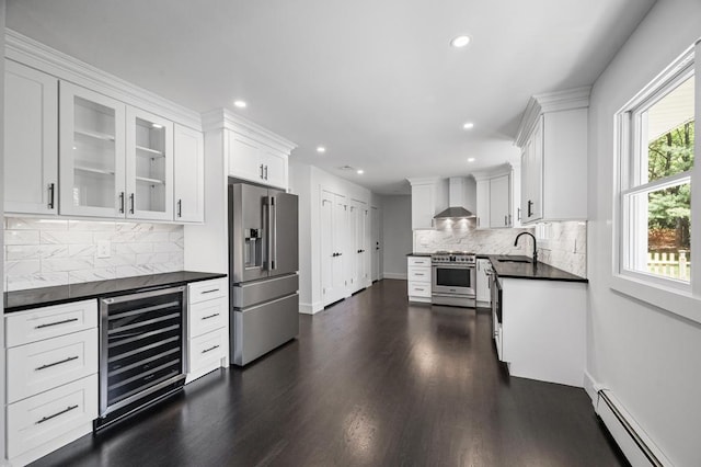 kitchen with wall chimney range hood, dark countertops, baseboard heating, wine cooler, and premium appliances