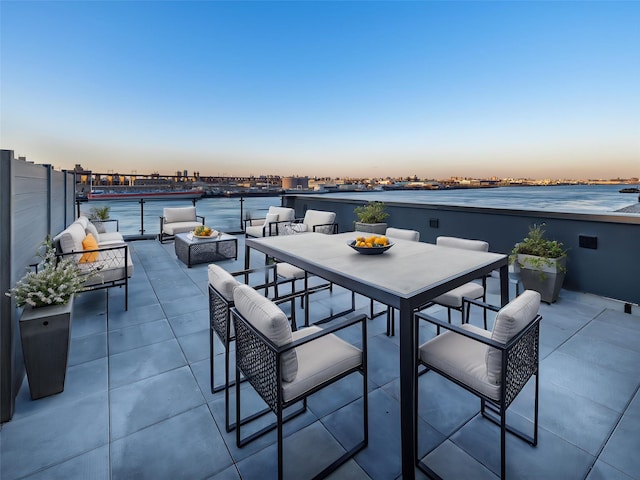 patio terrace at dusk featuring outdoor dining space, a water view, and an outdoor living space