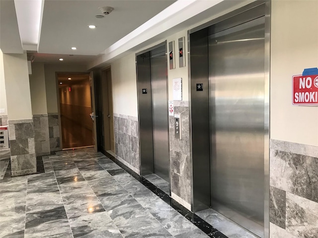 65-38 Austin St Unit 3B, Rego Park, NY 11374 - hall featuring tile walls, elevator, wainscoting, recessed lighting, and marble finish flooring