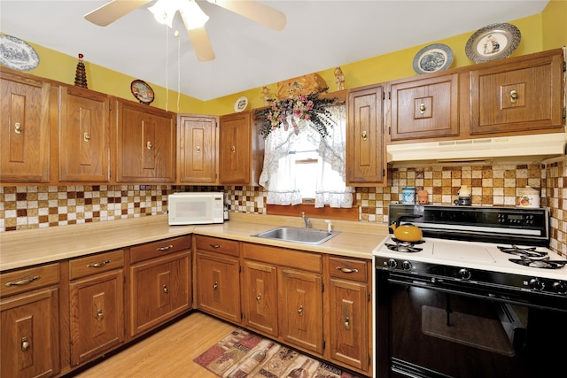 kitchen with range with gas stovetop, white microwave, light countertops, under cabinet range hood, and a sink
