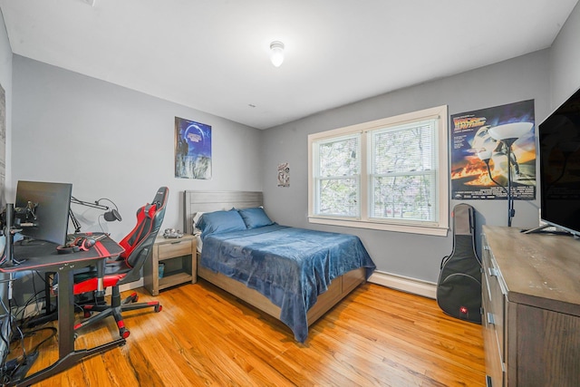 bedroom featuring a baseboard heating unit, baseboards, and light wood finished floors